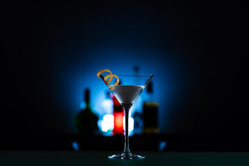Vertical shot of a martini in a cocktail glass served with orange peel against the bar background