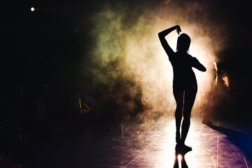 Plakat silhouette of a woman dancing between lights and smoke