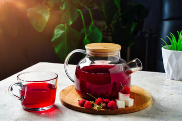 Herbal tea with red berries, raspberries in glass teapot and cup on table. Honey Medicine tea for...