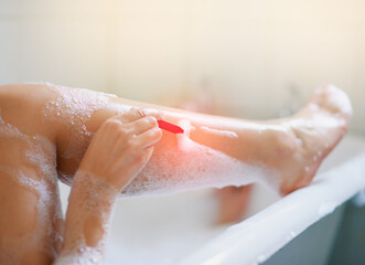 Fototapeta premium Keeping her legs silky smooth. Cropped shot of a woman shaving her legs while taking a bath.