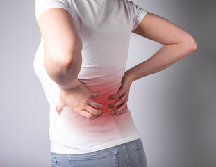 Woman suffering from backache. Hands holding lower back with red spot closeup. Health and medicine...