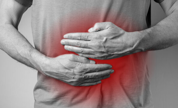 Man suffering from stomachache and holding hands on stomach with red spot closeup. Health and medicine concept. Indigestion, inflammation. High quality photo