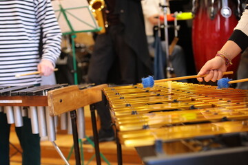 A person with hammers in his hands plays percussion in a youth jazz band with a player on saxophone drums piano rehearsing a concert standing on the school stage