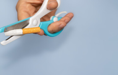 one cigarette through the blades of a scissors for kids. white and blue color scissors for child's activities. stop smoking concept. take down national day of action. world no tobacco day. free space