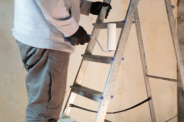 The builder starts painting with the help of a roller.Folding ladder for construction.