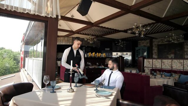 In The Restaurant, The Client Accepts The Order Of A Stylish Man In An Elite Restaurant. Customer service. A waiter who gives recommendations in a restaurant. The client reads the menu