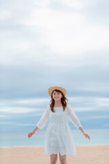 Fototapeta na wymiar 砂浜で麦わら帽子をかぶった笑顔の女性