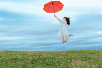 草原で傘を持ってジャンプする女性