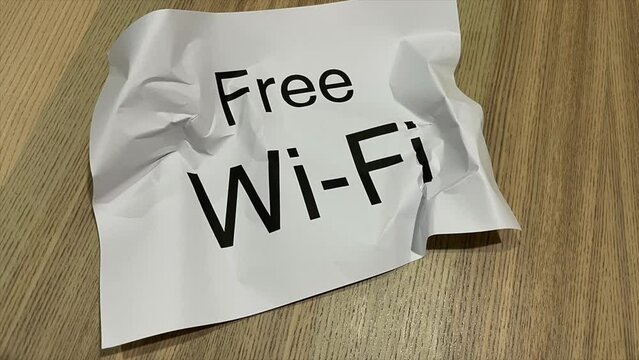 Paper crumpled into ball in stop motion animation paper wrinkle printed black text &ldquo;Free Wi-Fi&rdquo; on a wooden table background - close up shot