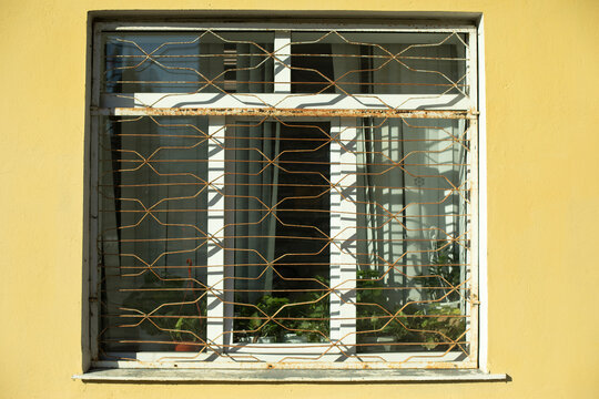 Window with grille. Ground floor of building. Window in yellow wall.