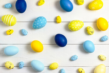 Easter eggs of different sizes, yellow and blue, lie on a white wooden table in the form of a pattern. Copy space, flat lay
