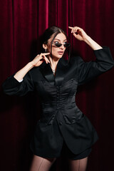 A model wearing all black posing in front of a red cinema curtain