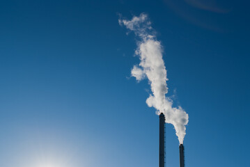 factory pipes against the blue sky. white smoke comes out of metal pipes.