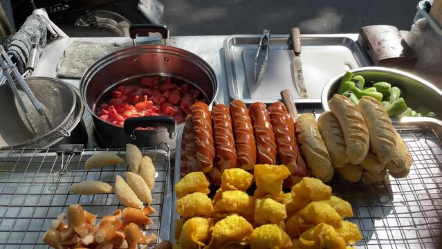 Cooking sausages street food vendor at road side on a sunny day near Chatuchak Weekend Market, largest weekend market in Thailand. Point of view shot red sausage boiling and cooked sausages on tray
