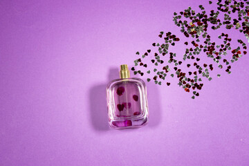 Perfume bottle with heart confetti on purple background