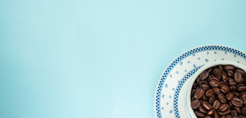 Many coffee beans in a traditional cup on blue background