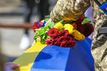 POLTAVA, UKRAINE - MARCH 24, 2022: A soldier holds flowers on a grave covered with the flag of Ukraine during the burial ceremony of fallen soldiers of the Armed Forces of Ukraine