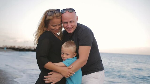Happy parents hug their beloved son on the seashore. Family values.