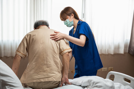 Attractive Young Asian Female Nurse Wearing Face Mask Take Care  Senior Patient In Hospital Bed Talking, Smiling And Cheering Up In Comfort At Hospital. Senior Healthcare And Medicine Concept.