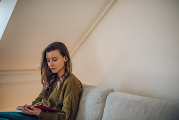 Woman reading a book while sitting on the couch at home