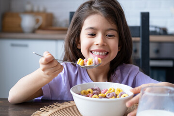 Happy arab child girl having breakfast colorful cereal with milk at home on the morning