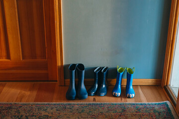Three pairs of blue rainboots are lined up against a wall next to a door
