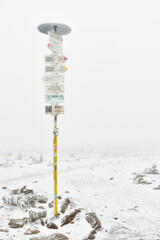 Frosted tourist signpost at the top of Mount Snieznik on a hiking mountain trail, winter landscape on a foggy day.