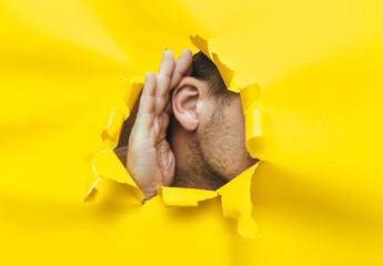 Right male ear and hands close-up. Copy space. Torn paper, yellow background. The concept of...