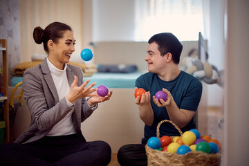 Playful man with down syndrome and his therapist have fun with plastic ball at home.