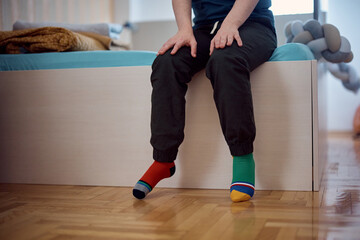 Unrecognizable down syndrome man with different color socks at home.