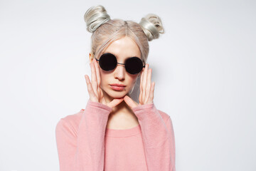 Fashionable pretty blonde girl with hair buns and sunglasses, on white.