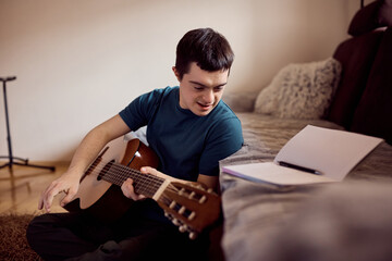 Smiling man with down syndrome enjoys in playing music on acoustic guitar at home.