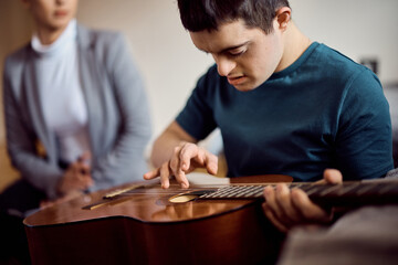 Down syndrome man playing acoustic guitar at home.