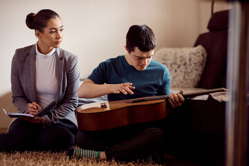 Man with down syndrome plays guitar during therapy with psychologist at home.