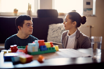 Young man with down syndrome talks to therapist while playing with toy blocks at home.