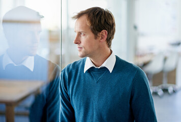 Hard decisions require harder thought. Shot of a handsome businessman looking through a glass window in an office.