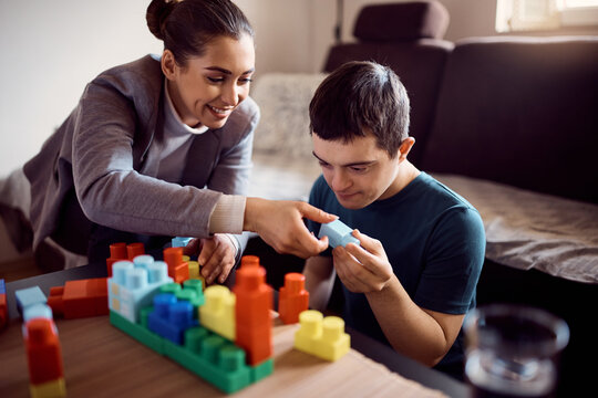 Man with down syndrome enjoys while stacking toy blocks with his psychologist at home.