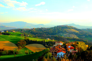 Wonderful view from above at colored houses and scenic hills covered with fields and forests under the blue sky with some light clouds in Monte Vidon Corrado
