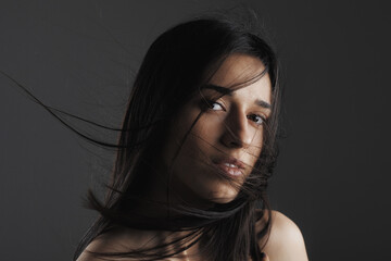 beauty fashion studio portrait of a beautiful young girl with windy hair in front of her face.