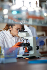 A young female student working with a microscope in a laboratory. Science, chemistry, lab, people - 495008920