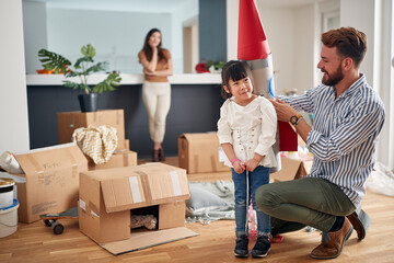 dad playing with a daughter, putting paper rocket on her back, with mom in the background watching.
