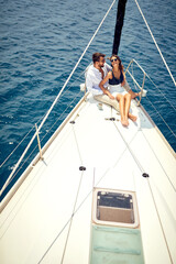 A young couple in love is sitting in a hug on the bow of the yacht and having a good time while ride on the sea. Summer, sea, vacation, relationship