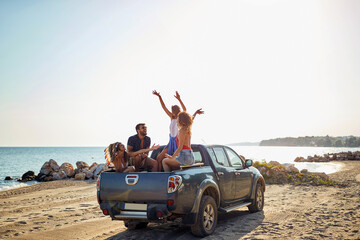 A group of handsome models is having a good time in the back of a car by the sea while listening to...