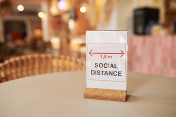 Naklejka na ściany i meble Close-up no people shot of sign with Social Distance text on modern cafe table, copy space