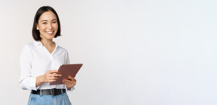 Image of young ceo manager, korean working woman holding tablet and smiling, standing over white background