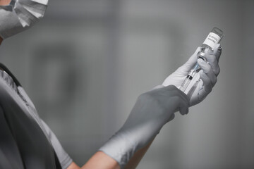 Close-up shot of unrecognizable medical worker wearing personal protection equipment filling syringe with Covid-19 vaccine, copy space