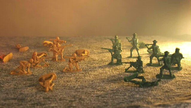 Two groups of toys opposite each other in smoke against a background of flickering light. Plastic soldiers fall in turn. The concept of human losses in the war