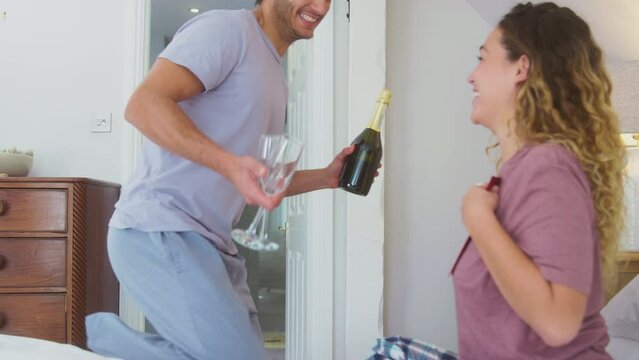 Loving couple wearing pyjamas in bed at home celebrating birthday, anniversary or valentines day with champagne as man gives woman card -  shot in slow motion