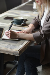 a business young beautiful woman sits at a table in a cafe waiting for an order, in front of her is a laptop in which she works on the Internet and makes notes in a notebook