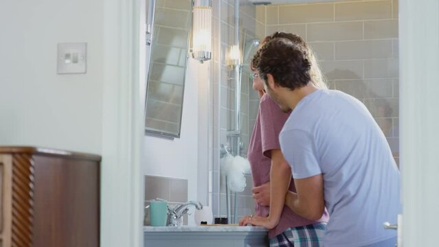 Man hugging woman wearing pyjamas in en suite bathroom as she brushes her teeth - shot in slow motion